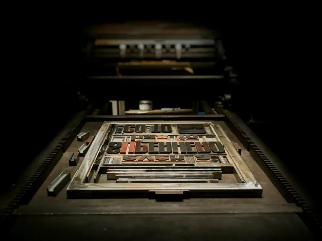 A chase of type locked up on the bed of a press, lit from one side