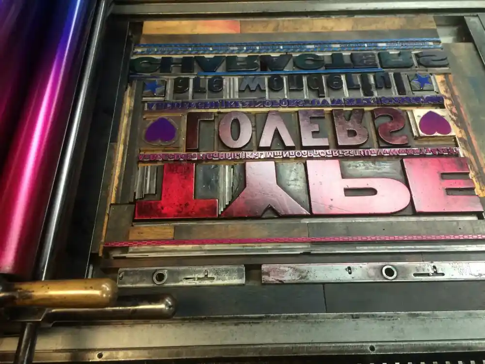 Wood type locked in a chase on the press bed, inked in red and violet
